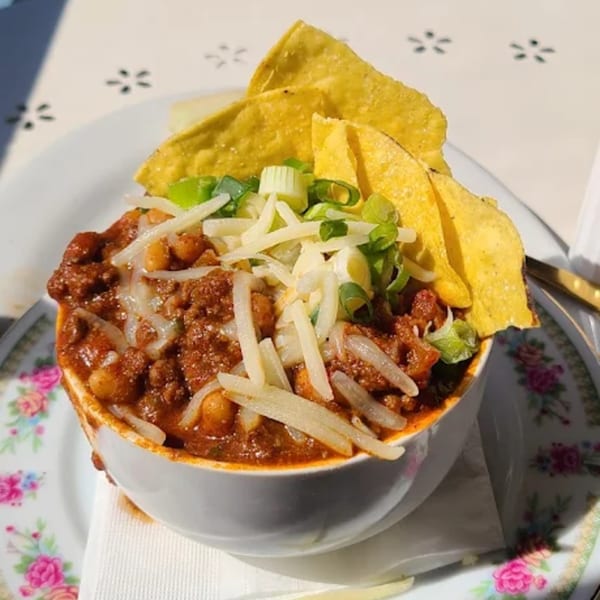 Hearty chili with shredded cheese, green onions, and tortilla chips in a white bowl on a floral plate.