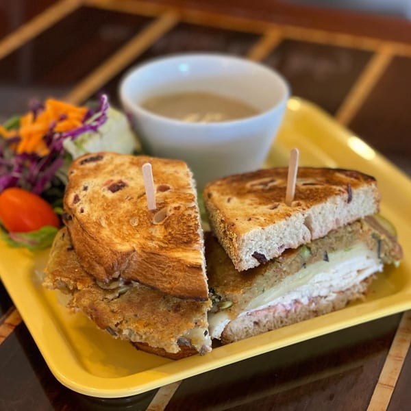 A grilled sandwich, cut in half, with a side salad and a cup of soup on a yellow tray.