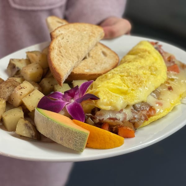 A breakfast plate with a cheesy omelet, home fries, toast, cantaloupe, orange slice, and a purple orchid.