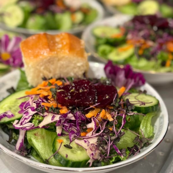 A fresh garden salad with cucumber, shredded carrots, red cabbage, and a bread roll.