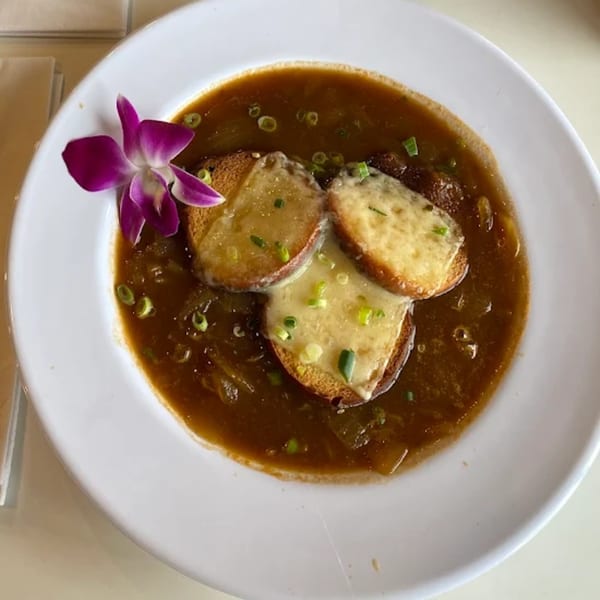 French onion soup with melted cheese croutons and a purple orchid garnish in a white bowl.