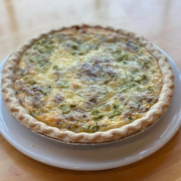 A whole quiche with a golden crust, filled with eggs, cheese, and green vegetables, on a white plate.