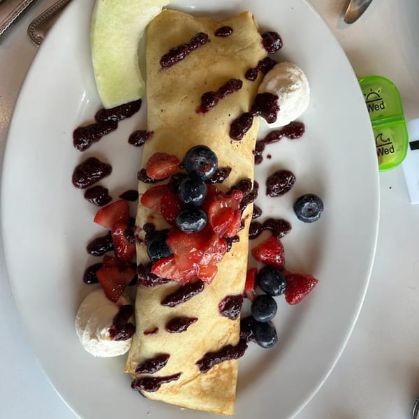 A breakfast crepe topped with berries, berry sauce, whipped cream, and a melon slice.