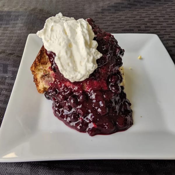 A slice of French toast topped with blueberry compote and a dollop of whipped cream.
