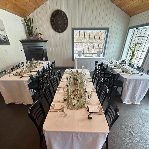 Dining room at For the Love of Food + Drink with set tables, white tablecloths, and large windows.