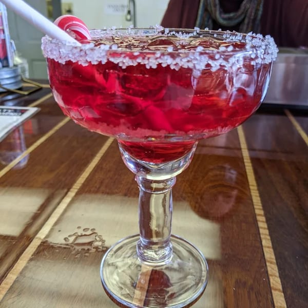 A red drink in a sugar-rimmed glass with a candy cane and straw on a wooden table.