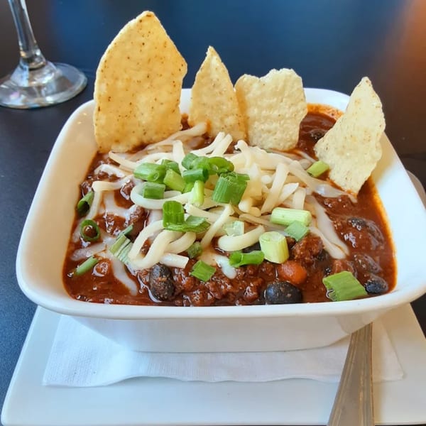 Hearty chili topped with shredded cheese, green onions, and tortilla chips in a white bowl.
